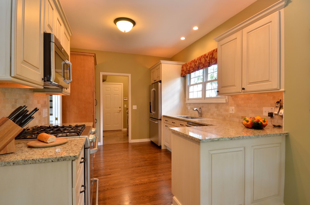 Mid-sized elegant galley medium tone wood floor kitchen photo in Chicago with an undermount sink, raised-panel cabinets, white cabinets, granite countertops, beige backsplash, stone tile backsplash and stainless steel appliances