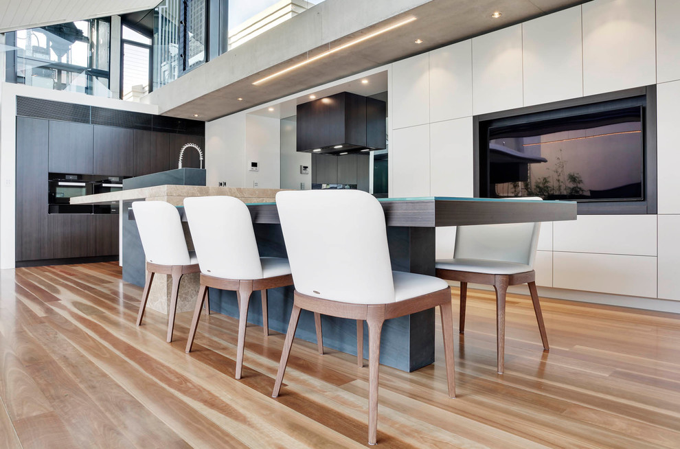 This is an example of an expansive modern l-shaped kitchen/diner in Sydney with a submerged sink, flat-panel cabinets, beige cabinets, marble worktops, grey splashback, glass sheet splashback, black appliances, medium hardwood flooring and an island.