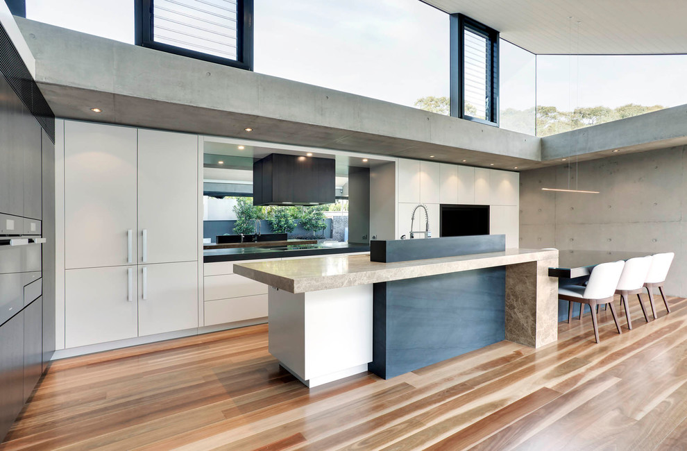 Geräumige Moderne Wohnküche in L-Form mit Unterbauwaschbecken, flächenbündigen Schrankfronten, beigen Schränken, Marmor-Arbeitsplatte, Küchenrückwand in Grau, Glasrückwand, braunem Holzboden und Kücheninsel in Sydney
