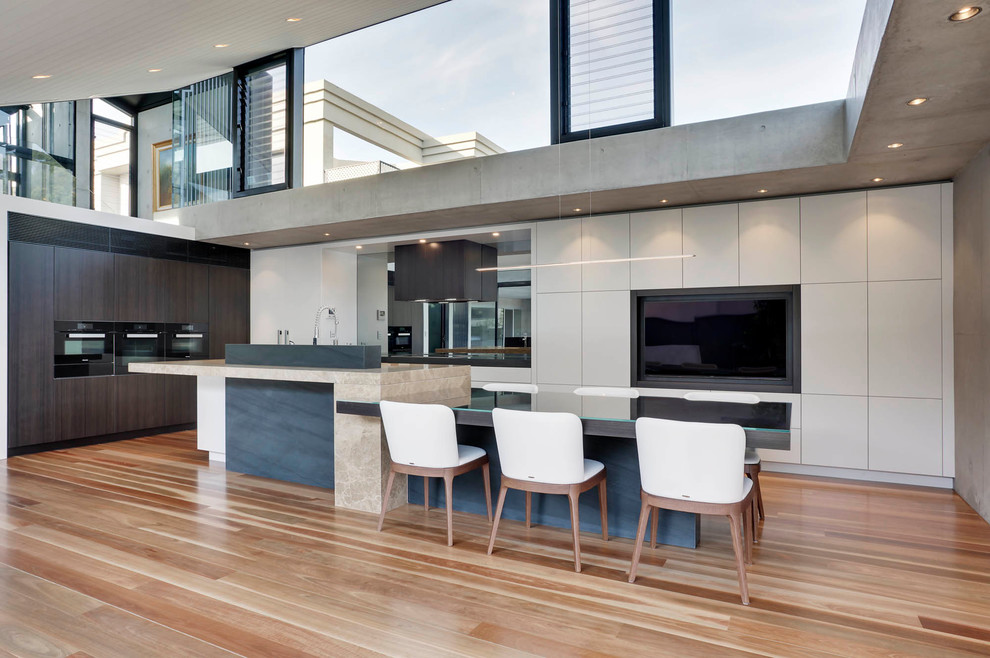 Geräumige Moderne Wohnküche in L-Form mit flächenbündigen Schrankfronten, weißen Schränken, Marmor-Arbeitsplatte, schwarzen Elektrogeräten, braunem Holzboden und Kücheninsel in Sydney