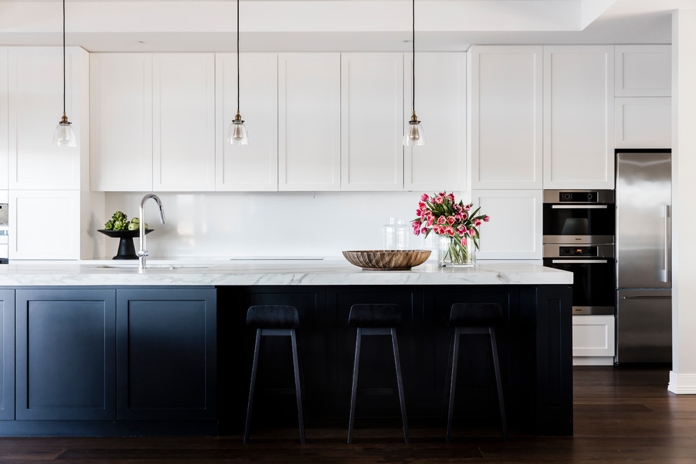 Exemple d'une cuisine parallèle chic avec un évier encastré, un placard à porte shaker, une crédence blanche, parquet foncé et îlot.