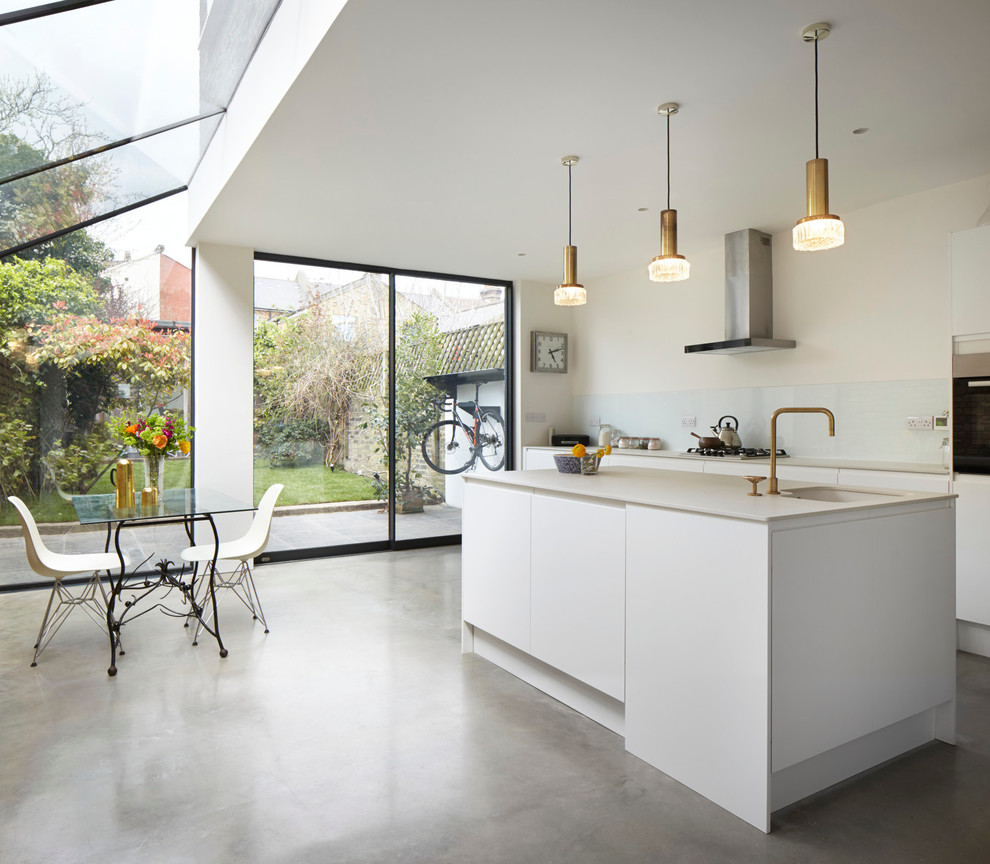 Inspiration for a small contemporary single-wall open plan kitchen in London with a belfast sink, flat-panel cabinets, white cabinets, composite countertops, white splashback, glass sheet splashback, white appliances, concrete flooring and an island.