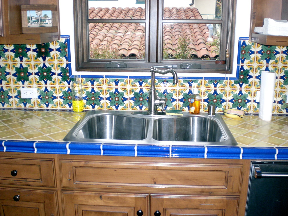 Example of a mid-sized tuscan u-shaped eat-in kitchen design with no island, flat-panel cabinets, dark wood cabinets, tile countertops, stainless steel appliances, a drop-in sink, multicolored backsplash and mosaic tile backsplash