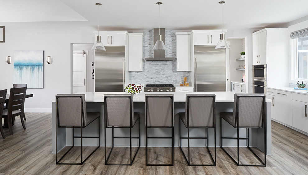 Transitional l-shaped medium tone wood floor and gray floor kitchen photo in Grand Rapids with flat-panel cabinets, white cabinets, quartzite countertops, gray backsplash, ceramic backsplash, stainless steel appliances, an island and white countertops