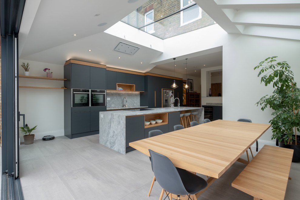 Bild på ett stort funkis grå grått kök och matrum, med släta luckor, grå skåp, marmorbänkskiva, grått stänkskydd, stänkskydd i marmor, rostfria vitvaror, en köksö och grått golv
