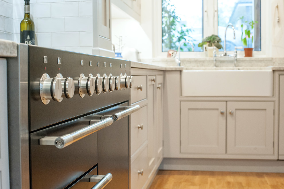 Inredning av ett klassiskt stort grå grått kök, med en dubbel diskho, skåp i shakerstil, grå skåp, granitbänkskiva, stänkskydd i stenkakel, rostfria vitvaror, ljust trägolv och beiget golv