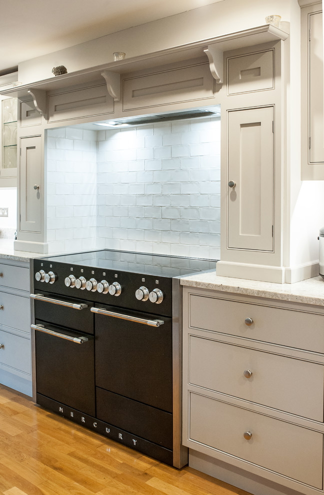 Klassisk inredning av ett stort grå grått kök, med en dubbel diskho, skåp i shakerstil, grå skåp, granitbänkskiva, stänkskydd i stenkakel, rostfria vitvaror, ljust trägolv och beiget golv