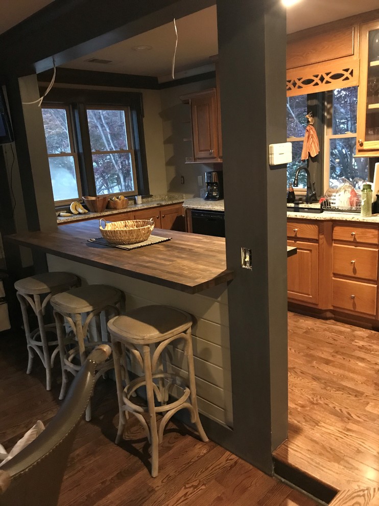 Foto på ett mellanstort amerikanskt u-kök, med mellanmörkt trägolv, brunt golv, en undermonterad diskho, luckor med upphöjd panel, skåp i mellenmörkt trä, träbänkskiva, svarta vitvaror och en halv köksö