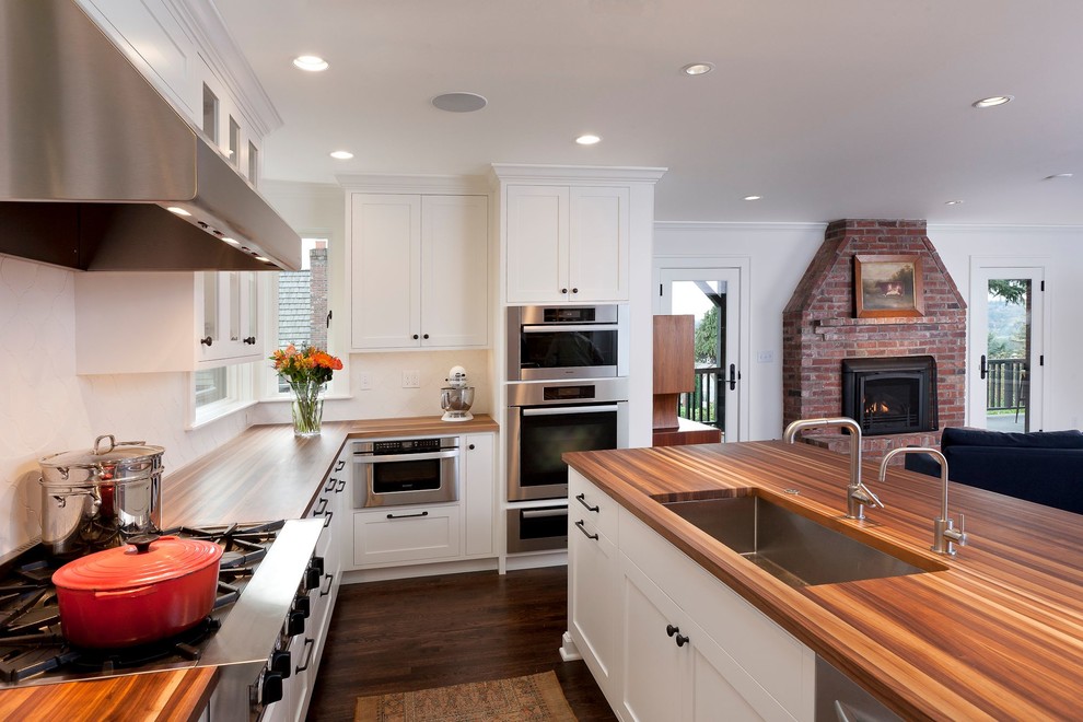 Large minimalist l-shaped dark wood floor and brown floor eat-in kitchen photo in New York with an undermount sink, shaker cabinets, white cabinets, wood countertops, white backsplash, stone tile backsplash, stainless steel appliances and an island