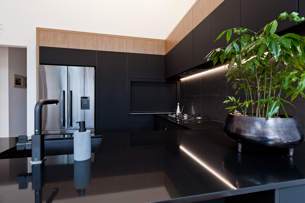 Design ideas for a medium sized industrial u-shaped open plan kitchen in Perth with a submerged sink, black cabinets, engineered stone countertops, black splashback, porcelain splashback, black appliances, medium hardwood flooring, a breakfast bar and black worktops.
