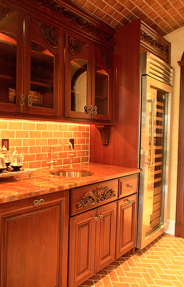 Inredning av ett amerikanskt litet kök, med skåp i mellenmörkt trä, granitbänkskiva, brunt stänkskydd, stänkskydd i tunnelbanekakel, tegelgolv, en undermonterad diskho, luckor med upphöjd panel och rostfria vitvaror