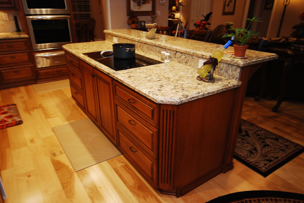 Example of a classic u-shaped eat-in kitchen design in Other with an undermount sink, raised-panel cabinets, medium tone wood cabinets, quartz countertops, beige backsplash, porcelain backsplash and stainless steel appliances