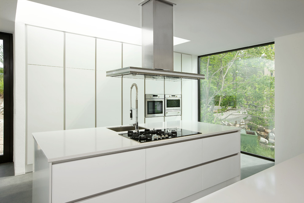Diseño de cocina comedor minimalista con fregadero bajoencimera, armarios con paneles lisos, puertas de armario blancas, encimera de cuarzo compacto y electrodomésticos de acero inoxidable