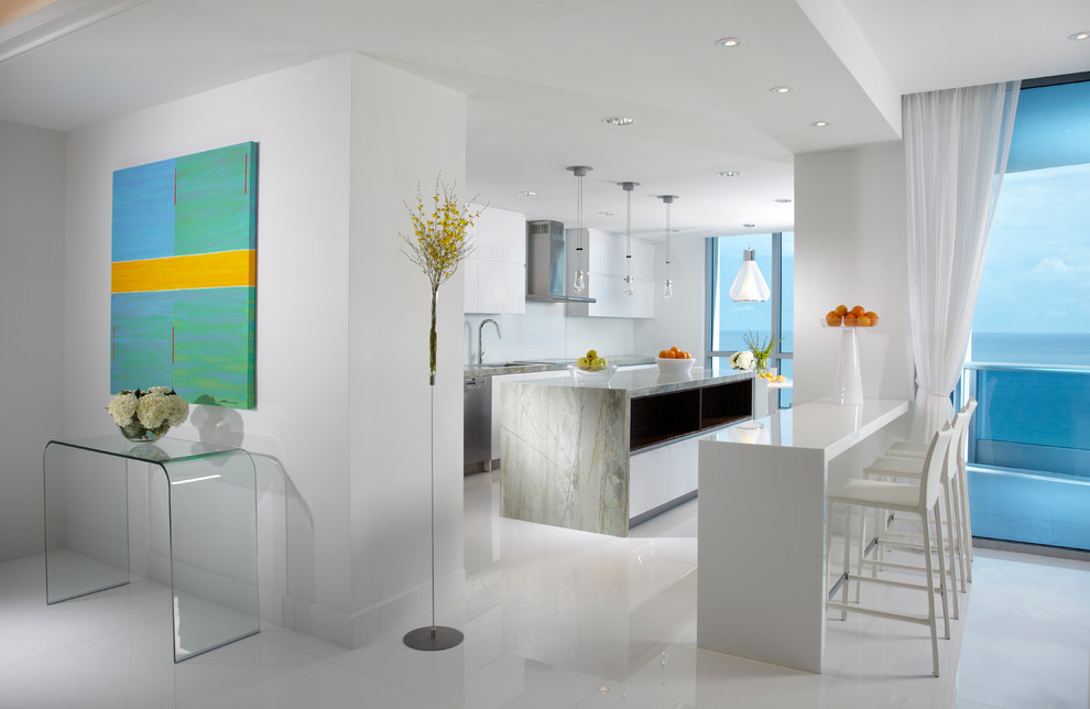 Photo of a large contemporary galley kitchen/diner in Miami with a double-bowl sink, white cabinets, marble worktops, white splashback, glass sheet splashback, stainless steel appliances, white floors, marble flooring, an island, grey worktops and flat-panel cabinets.