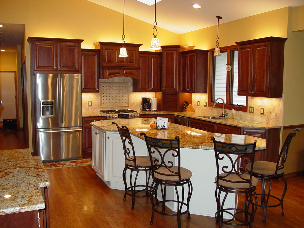 Inspiration for a large timeless l-shaped dark wood floor and brown floor eat-in kitchen remodel in Cleveland with an undermount sink, raised-panel cabinets, dark wood cabinets, granite countertops, beige backsplash, stone tile backsplash, stainless steel appliances and an island