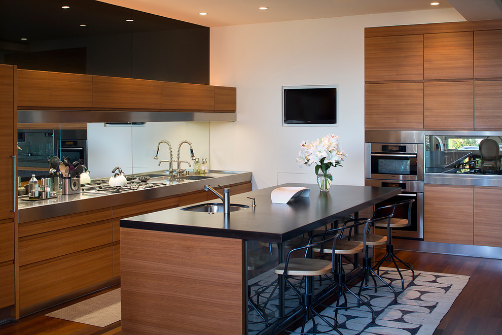 This is an example of a contemporary kitchen in San Francisco with flat-panel cabinets, medium wood cabinets, mirror splashback and stainless steel appliances.