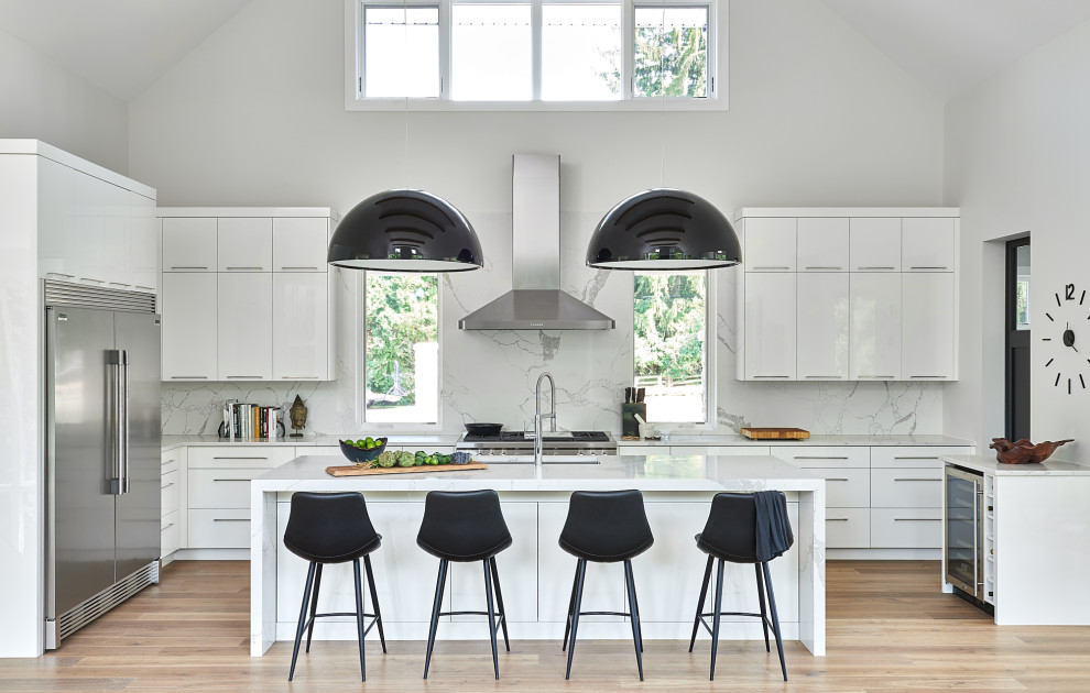 Kitchen - contemporary u-shaped medium tone wood floor, brown floor and vaulted ceiling kitchen idea in Toronto with an undermount sink, flat-panel cabinets, white cabinets, white backsplash, stainless steel appliances, an island and white countertops