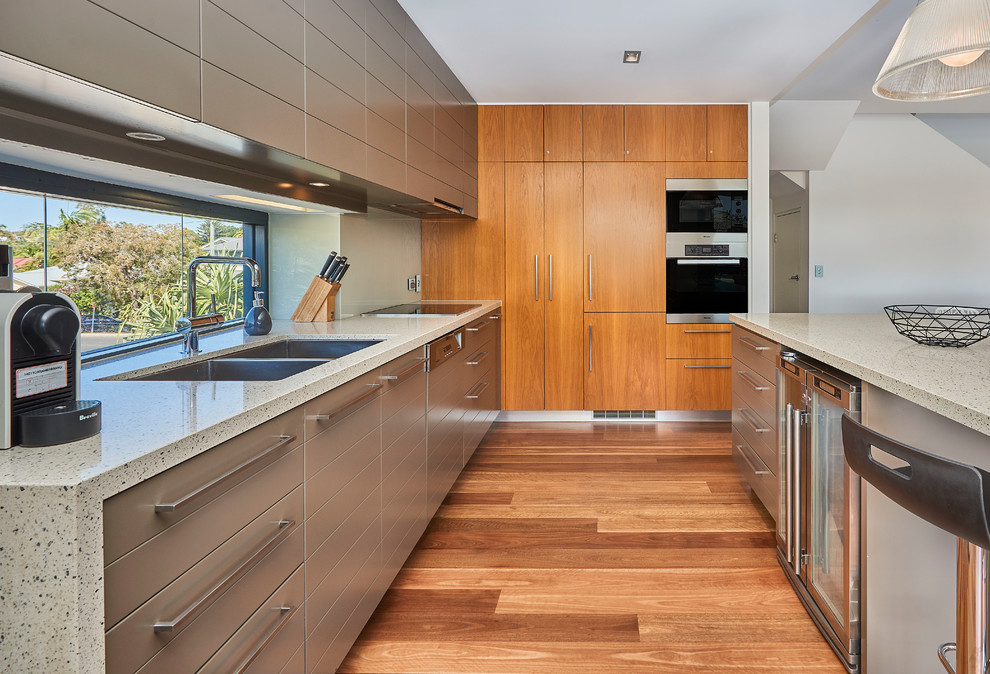 World-inspired l-shaped kitchen in Other with a submerged sink, flat-panel cabinets, brown cabinets, window splashback, stainless steel appliances, light hardwood flooring, an island, brown floors and beige worktops.