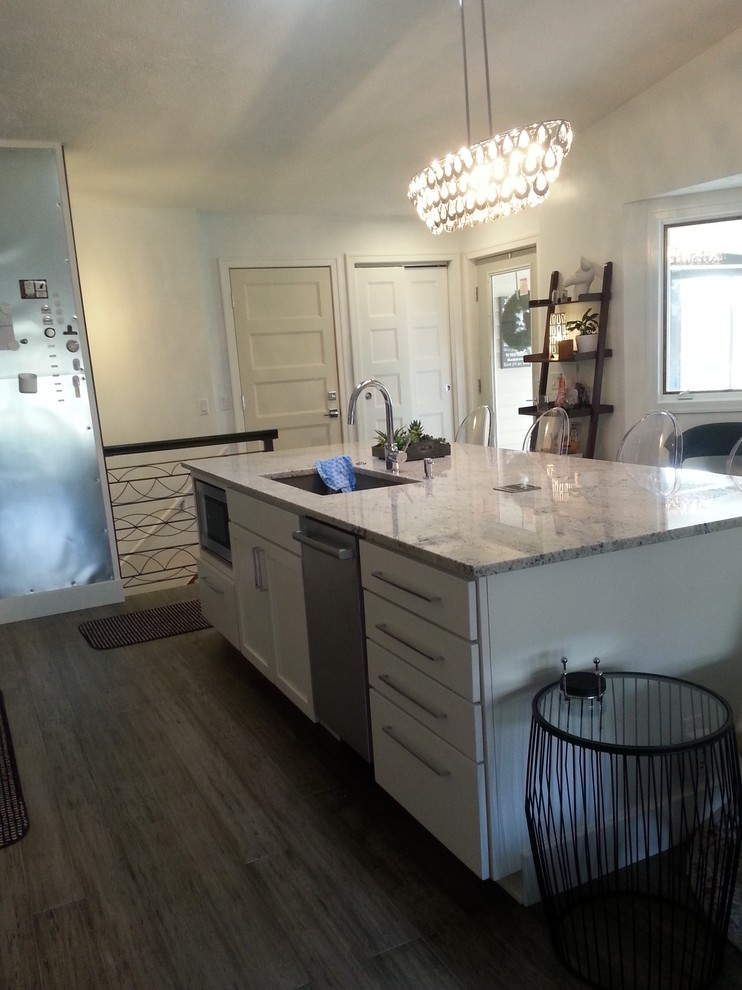 Exempel på ett litet klassiskt linjärt kök med öppen planlösning, med en enkel diskho, skåp i shakerstil, vita skåp, granitbänkskiva, vitt stänkskydd, stänkskydd i keramik, rostfria vitvaror, laminatgolv, en köksö och grått golv