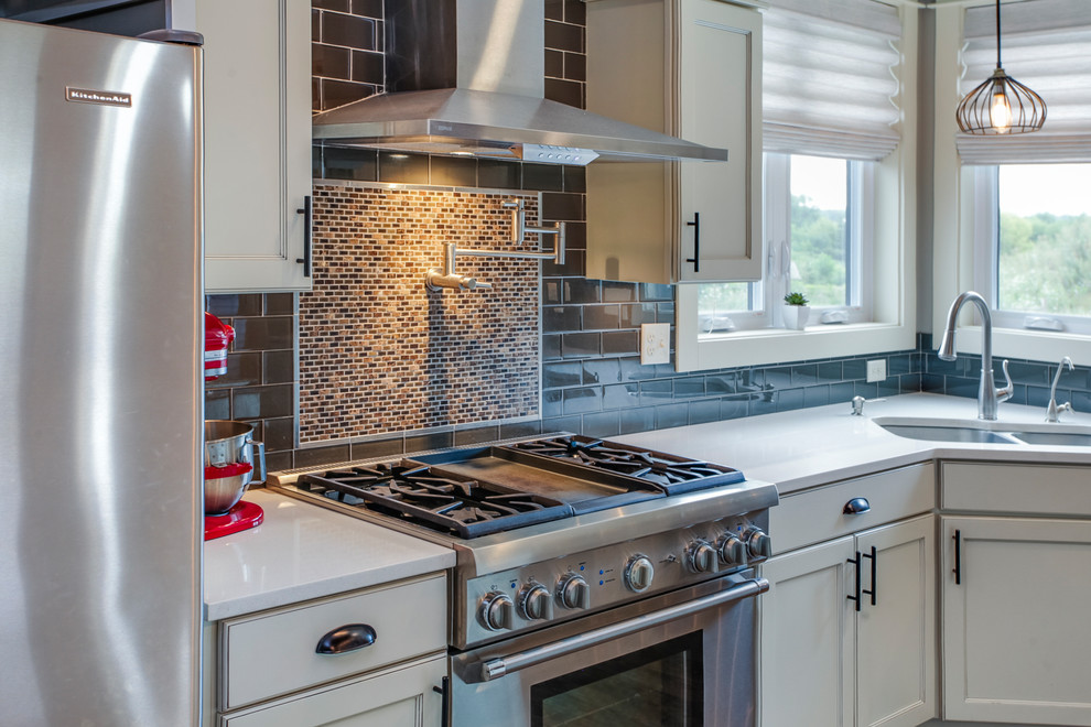 Amerikansk inredning av ett flerfärgad flerfärgat kök, med en undermonterad diskho, skåp i shakerstil, vita skåp, granitbänkskiva, svart stänkskydd, stänkskydd i keramik, rostfria vitvaror, laminatgolv, en köksö och brunt golv