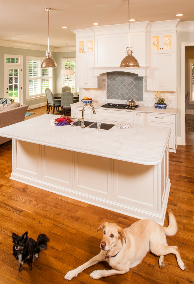 Exempel på ett mellanstort klassiskt kök, med en enkel diskho, luckor med profilerade fronter, vita skåp, marmorbänkskiva, vitt stänkskydd, stänkskydd i tunnelbanekakel, rostfria vitvaror, mellanmörkt trägolv och en köksö