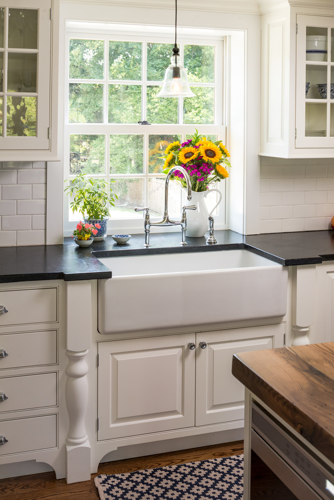 Eat-in kitchen - country u-shaped medium tone wood floor eat-in kitchen idea in Philadelphia with a farmhouse sink, glass-front cabinets, white cabinets, white backsplash, subway tile backsplash, stainless steel appliances, an island and granite countertops