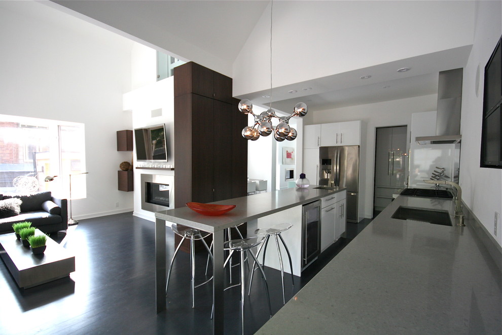 Пример оригинального дизайна: кухня-гостиная в стиле модернизм с техникой из нержавеющей стали, одинарной мойкой, плоскими фасадами, белыми фасадами и столешницей из кварцевого агломерата