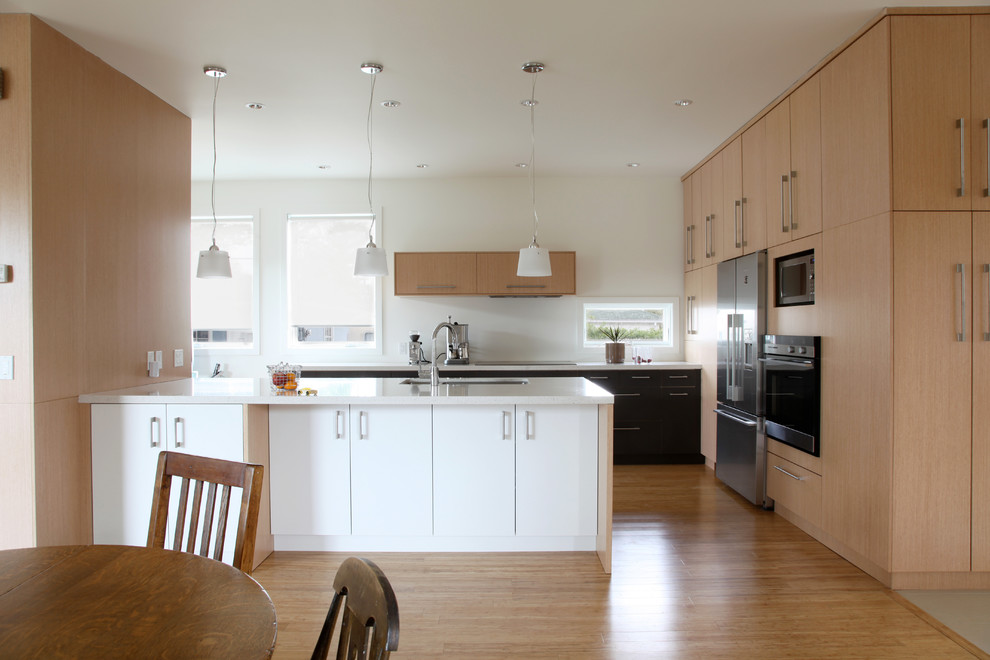 Zweizeilige Moderne Wohnküche mit Unterbauwaschbecken, flächenbündigen Schrankfronten, schwarzen Schränken, Quarzwerkstein-Arbeitsplatte, Küchengeräten aus Edelstahl und hellem Holzboden in Calgary