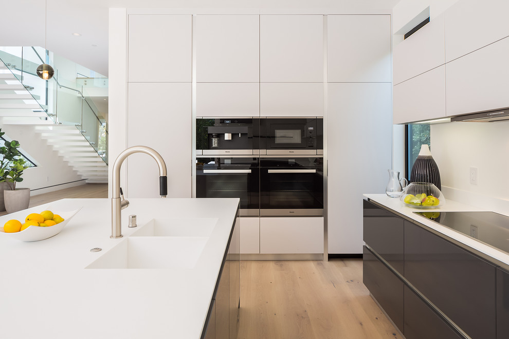 Esempio di un cucina con isola centrale design con lavello a doppia vasca, ante lisce, ante bianche, elettrodomestici neri e parquet chiaro