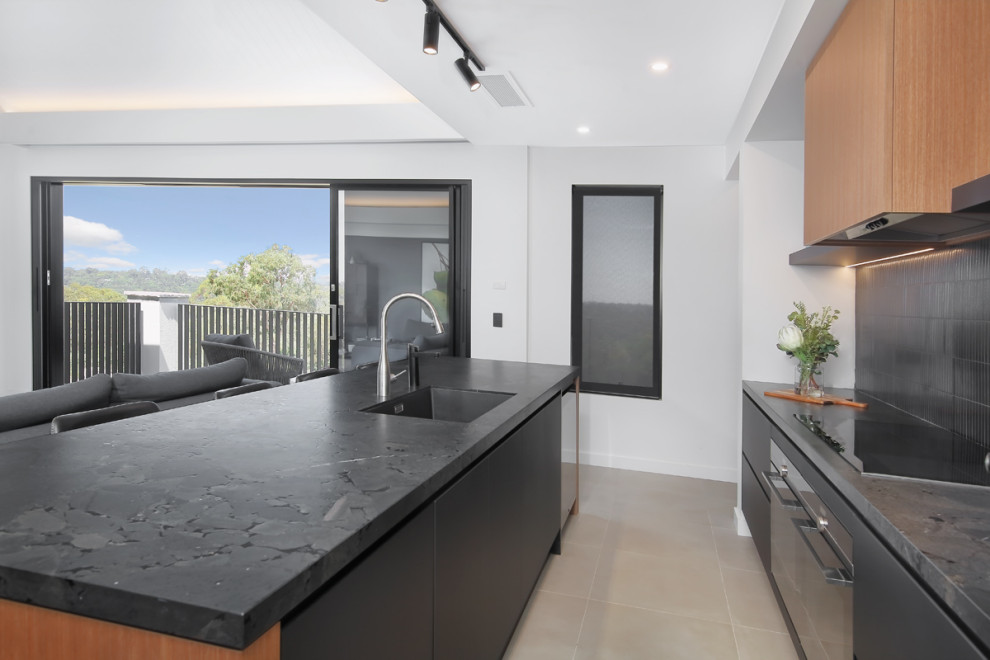 Example of a mid-sized trendy galley ceramic tile and beige floor open concept kitchen design in Sydney with an undermount sink, flat-panel cabinets, black cabinets, quartz countertops, black backsplash, cement tile backsplash, black appliances, an island and black countertops