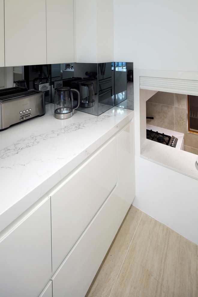 Diseño de cocina comedor moderna con armarios con paneles lisos, puertas de armario blancas, salpicadero blanco, salpicadero de losas de piedra, electrodomésticos negros y una isla