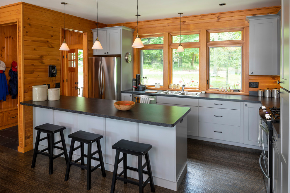Photo of a rustic l-shaped kitchen in Minneapolis with grey cabinets, engineered stone countertops, stainless steel appliances, black worktops, a double-bowl sink, flat-panel cabinets, window splashback, dark hardwood flooring, an island and brown floors.