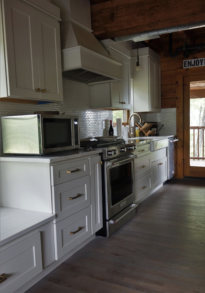 Cette image montre une cuisine américaine linéaire chalet avec un évier de ferme, un placard à porte shaker, une crédence blanche et un électroménager en acier inoxydable.