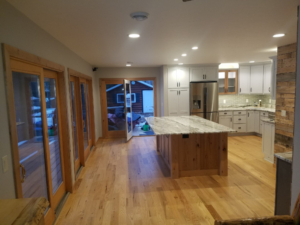 Mid-sized minimalist l-shaped medium tone wood floor and brown floor open concept kitchen photo in Other with an undermount sink, recessed-panel cabinets, white cabinets, granite countertops, gray backsplash, subway tile backsplash, stainless steel appliances, an island and white countertops