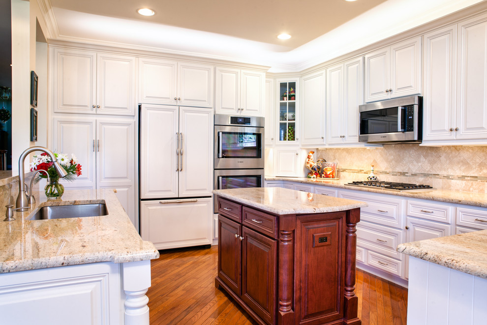 Bild på ett mellanstort vintage kök, med en undermonterad diskho, luckor med upphöjd panel, vita skåp, granitbänkskiva, beige stänkskydd, stänkskydd i stenkakel, rostfria vitvaror, mellanmörkt trägolv och en köksö