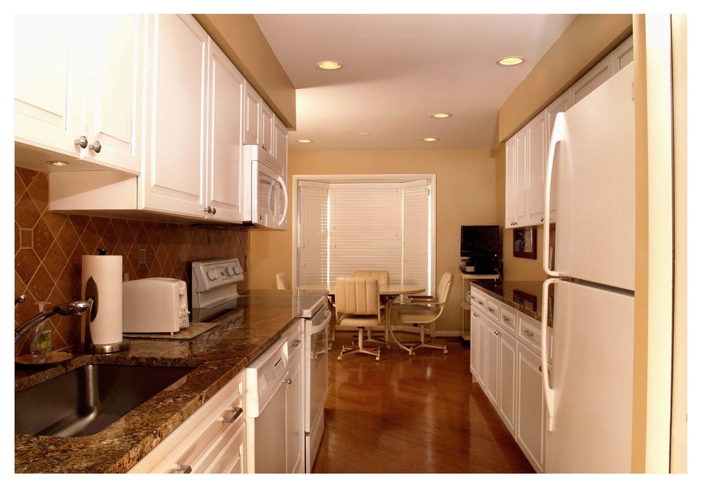 Example of a transitional galley eat-in kitchen design in Baltimore with raised-panel cabinets, white cabinets, granite countertops, brown backsplash, white appliances and no island