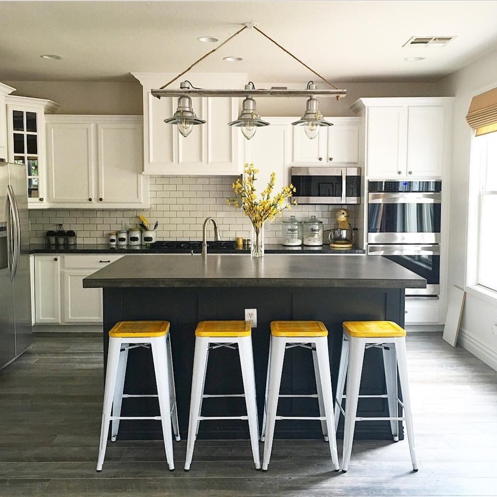 Inspiration for a classic l-shaped kitchen in Phoenix with recessed-panel cabinets, white cabinets, white splashback, metro tiled splashback, stainless steel appliances, an island and grey floors.