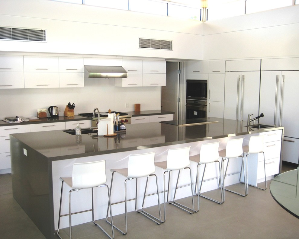 Example of a large trendy l-shaped concrete floor open concept kitchen design in Los Angeles with an undermount sink, flat-panel cabinets, white cabinets, quartz countertops, white backsplash, glass sheet backsplash, paneled appliances and an island