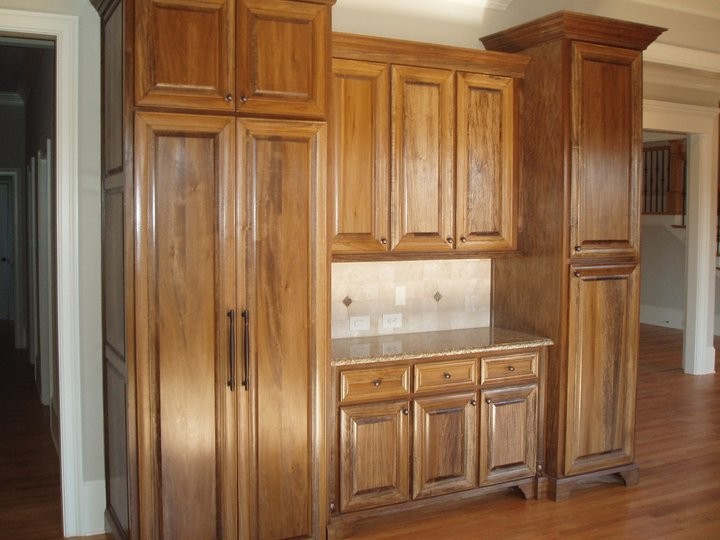 Cette image montre une cuisine américaine traditionnelle en bois brun avec un placard avec porte à panneau surélevé, un plan de travail en granite, une crédence beige, une crédence en carrelage de pierre, un sol en bois brun et aucun îlot.