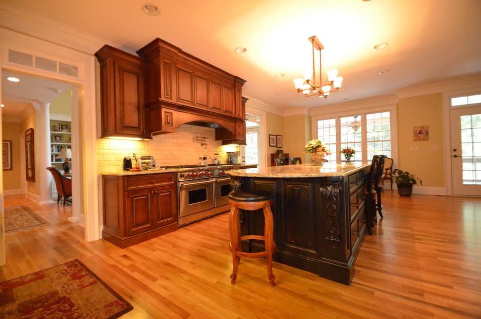 Example of a large classic l-shaped medium tone wood floor enclosed kitchen design in Atlanta with an undermount sink, dark wood cabinets, granite countertops, beige backsplash, subway tile backsplash and stainless steel appliances