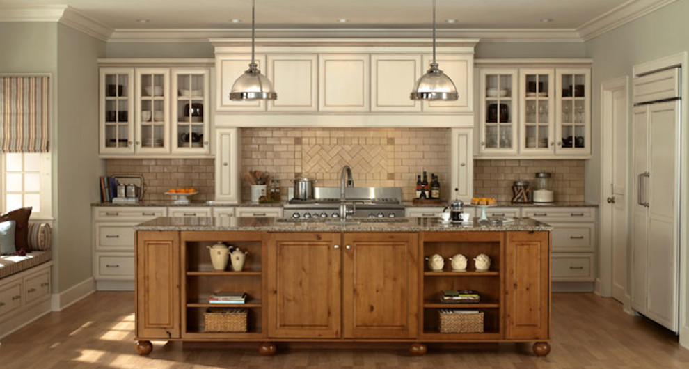 Example of a mid-sized farmhouse l-shaped medium tone wood floor and brown floor kitchen design in Houston with an undermount sink, recessed-panel cabinets, white cabinets, granite countertops, brown backsplash, paneled appliances and an island