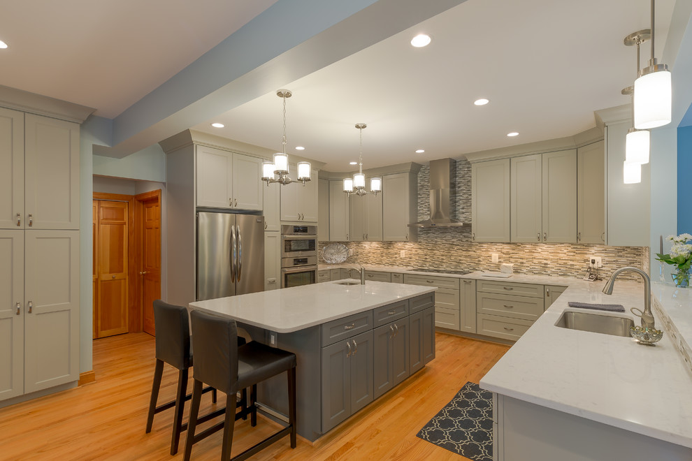 This is an example of a large traditional u-shaped kitchen/diner in DC Metro with an island, a submerged sink, shaker cabinets, grey cabinets, quartz worktops, grey splashback, glass tiled splashback, stainless steel appliances, medium hardwood flooring and brown floors.