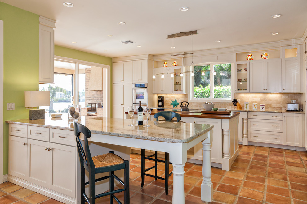 Photo of a classic u-shaped kitchen in Other with recessed-panel cabinets, beige cabinets, beige splashback, stainless steel appliances, terracotta flooring, an island, brown floors and brown worktops.
