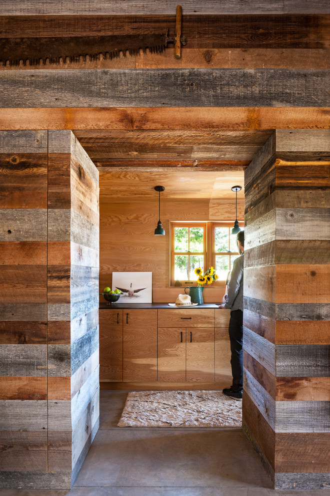 Aménagement d'une cuisine parallèle montagne en bois brun fermée et de taille moyenne avec un placard à porte plane, sol en béton ciré, aucun îlot, plan de travail noir, une crédence en bois et un sol gris.