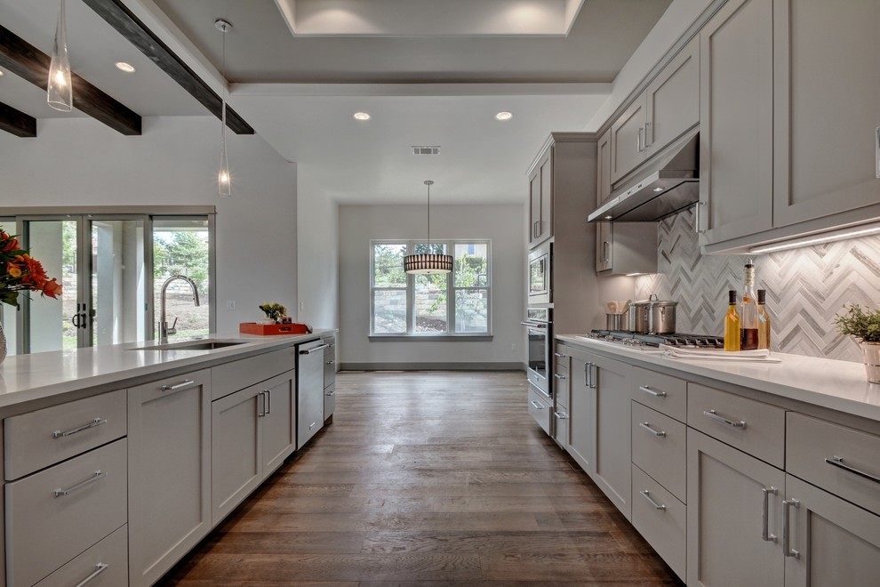 Open concept kitchen - large contemporary galley light wood floor and gray floor open concept kitchen idea in Austin with a single-bowl sink, shaker cabinets, gray cabinets, quartz countertops, white backsplash, marble backsplash, stainless steel appliances and an island