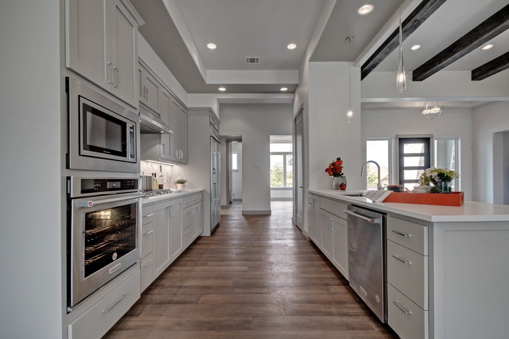 Idéer för att renovera ett stort funkis kök, med en enkel diskho, skåp i shakerstil, grå skåp, bänkskiva i kvarts, vitt stänkskydd, stänkskydd i marmor, rostfria vitvaror, ljust trägolv, en köksö och grått golv