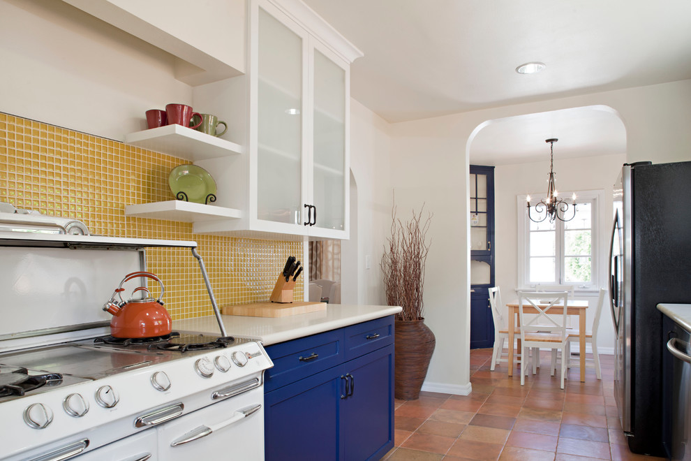 Inspiration for a medium sized eclectic galley enclosed kitchen in Los Angeles with a belfast sink, shaker cabinets, blue cabinets, yellow splashback, mosaic tiled splashback, white appliances, terracotta flooring and no island.
