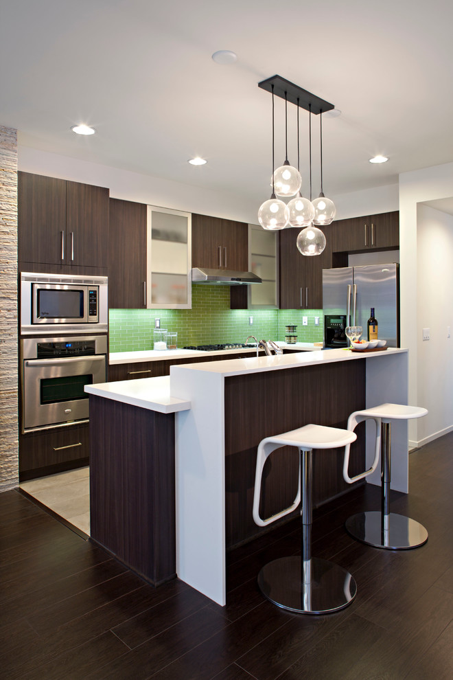 Example of a mid-sized trendy l-shaped dark wood floor open concept kitchen design in Los Angeles with stainless steel appliances, an undermount sink, flat-panel cabinets, dark wood cabinets, quartz countertops, green backsplash, subway tile backsplash and an island