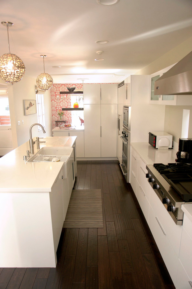 This is an example of a medium sized classic l-shaped kitchen/diner in Los Angeles with an integrated sink, glass-front cabinets, white cabinets, engineered stone countertops, white splashback, stainless steel appliances, dark hardwood flooring and an island.