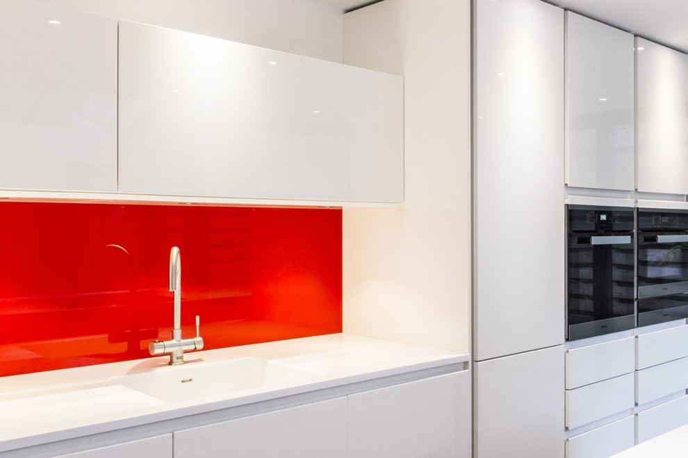 Bild på ett mellanstort funkis linjärt kök och matrum, med en integrerad diskho, släta luckor, vita skåp, bänkskiva i koppar, rött stänkskydd, glaspanel som stänkskydd, rostfria vitvaror, mörkt trägolv och en köksö